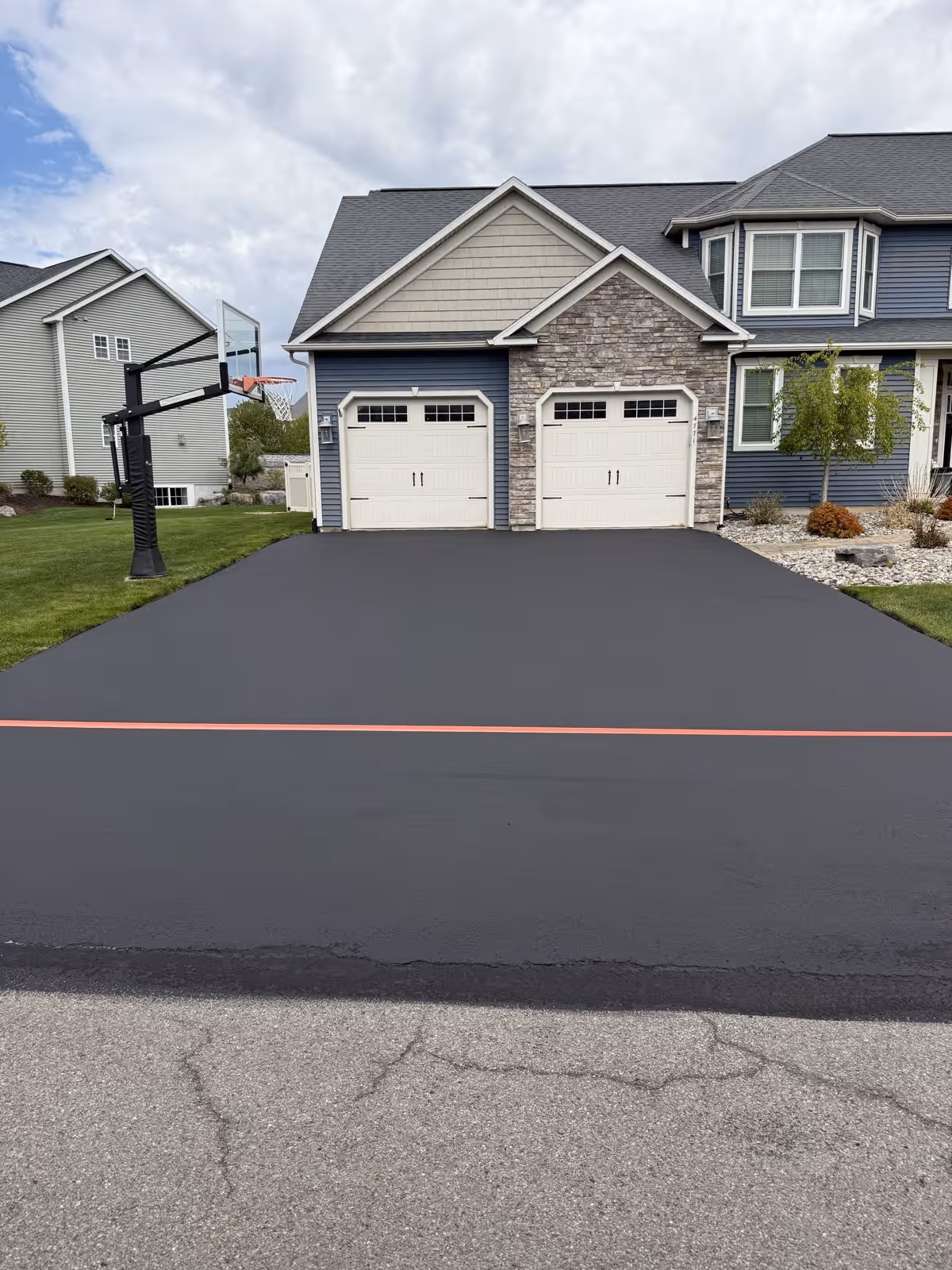 A wide fresh-black asphalt surface edged clean with a crisp red chalk line at a two-story property