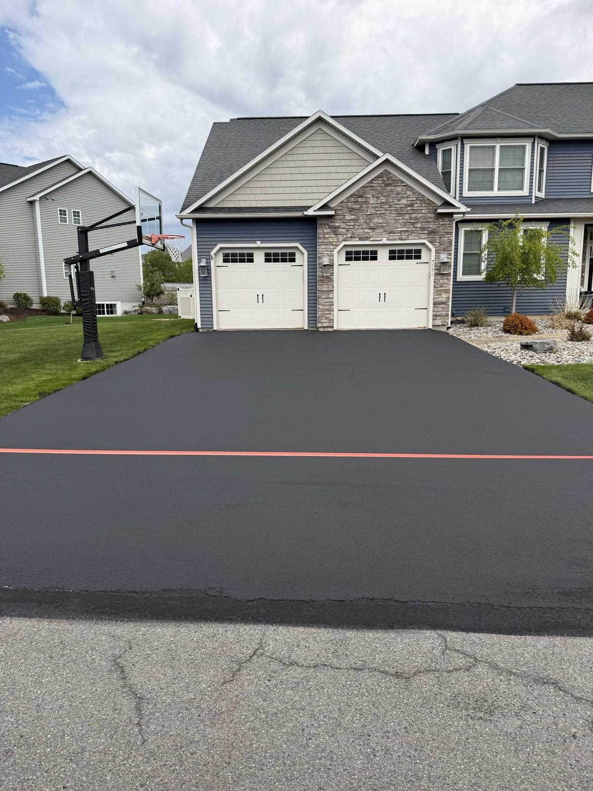 A wide fresh-black driveway at a two-story home, edged clean with a crisp red chalk line