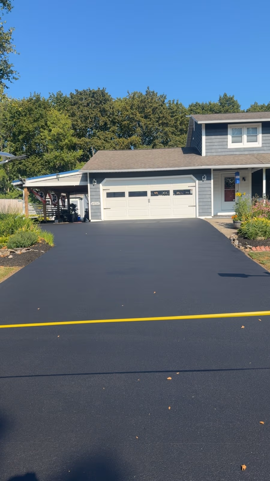 A freshly sealed jet-black driveway running up to a white garage under a clear blue sky