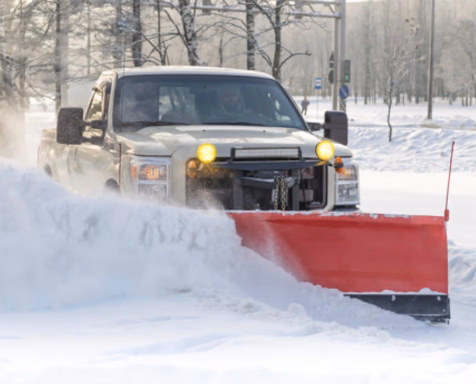 A plow truck with a red blade pushing deep snow off a parking lot